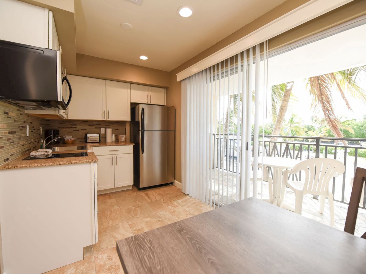 This image shows a modern kitchen with stainless steel appliances and a sliding door leading to a balcony with outdoor seating.