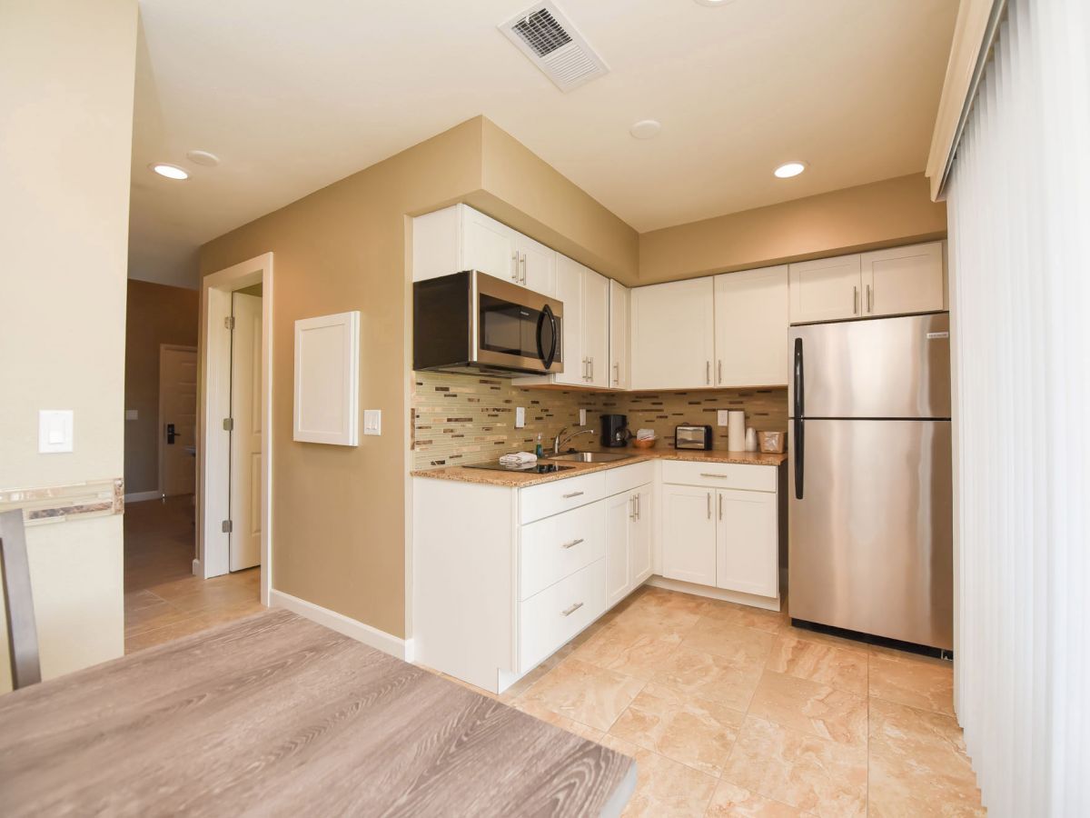 A modern kitchen with white cabinets, stainless steel appliances, a microwave, and a tiled backsplash. There's a table in the foreground.