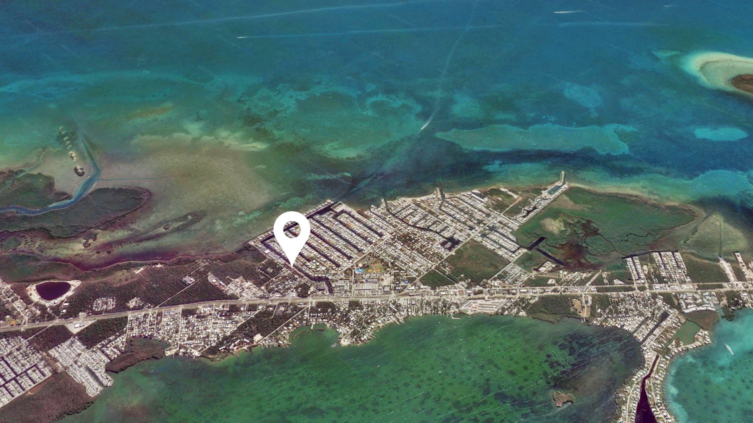 An aerial view of a coastal town with a pin drop location marker near the center of the image, indicating a specific place.