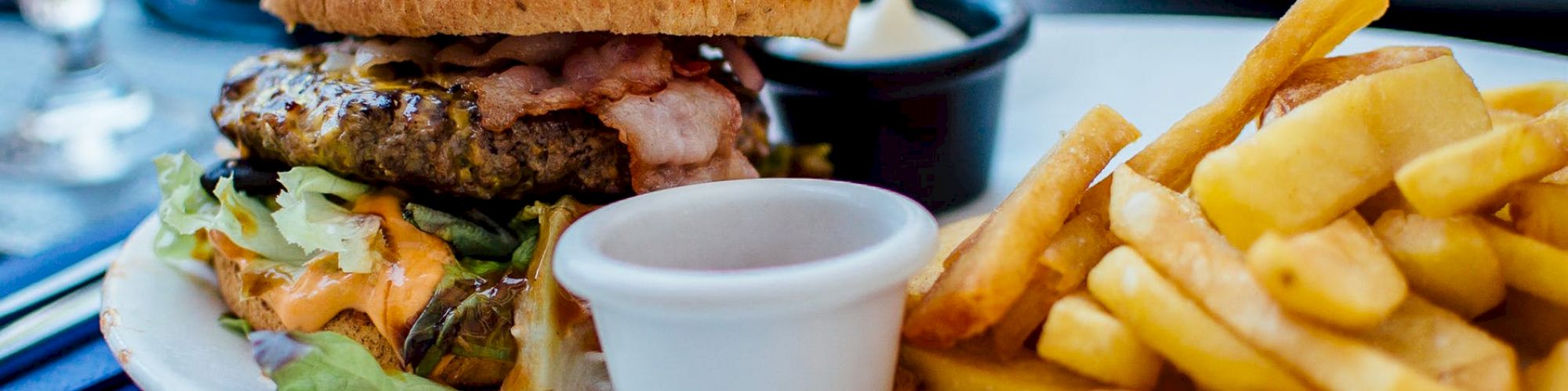 A plate with a burger containing lettuce and bacon, a serving of fries, and a small container of dipping sauce, all on a wooden table.