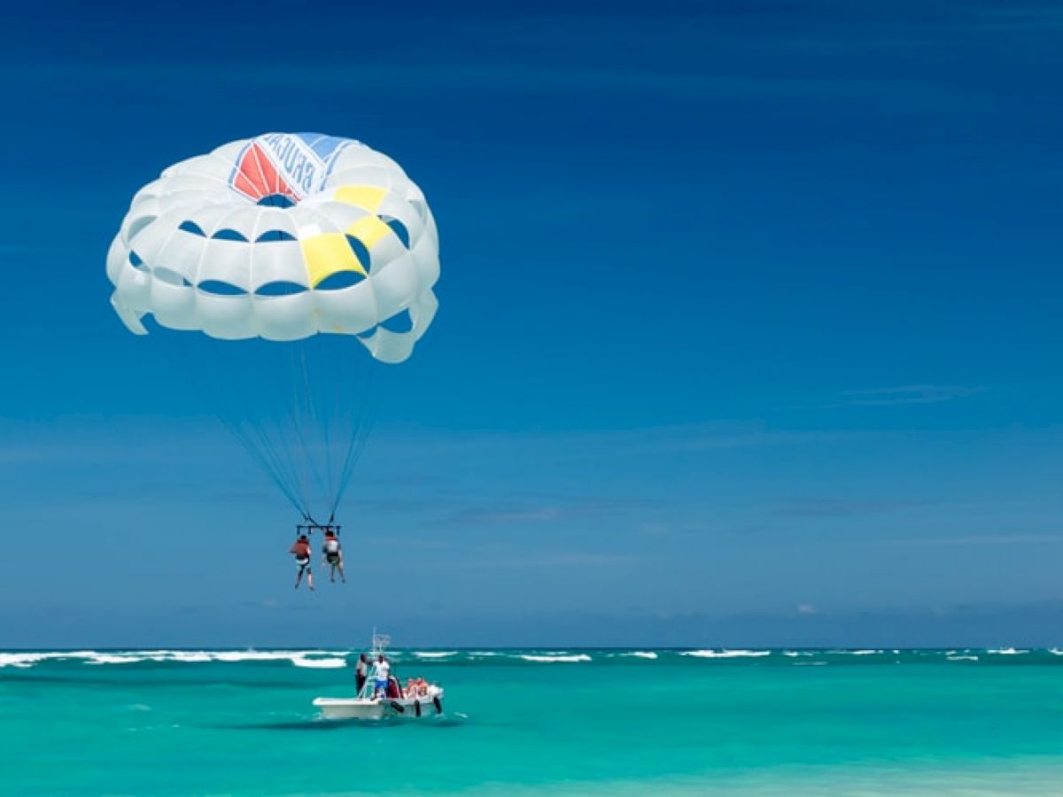 People are parasailing over clear blue ocean waters, attached to a parachute, with a boat pulling them in the distance.