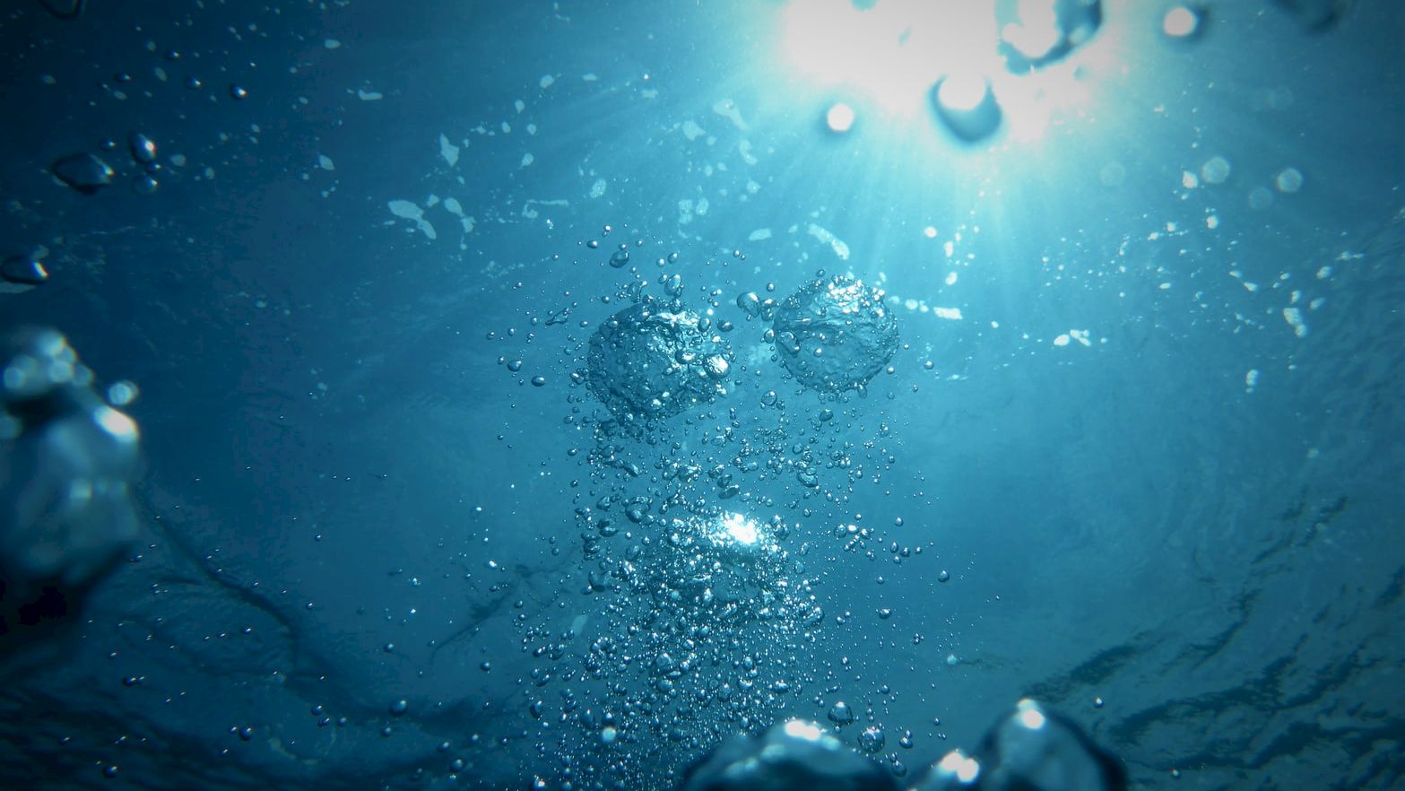 The image shows an underwater scene with bubbles rising towards a bright light source at the surface, creating a serene and mysterious atmosphere.