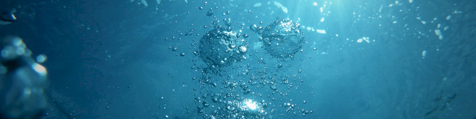 The image shows an underwater scene with bubbles rising towards a bright light source at the surface, creating a serene and mysterious atmosphere.