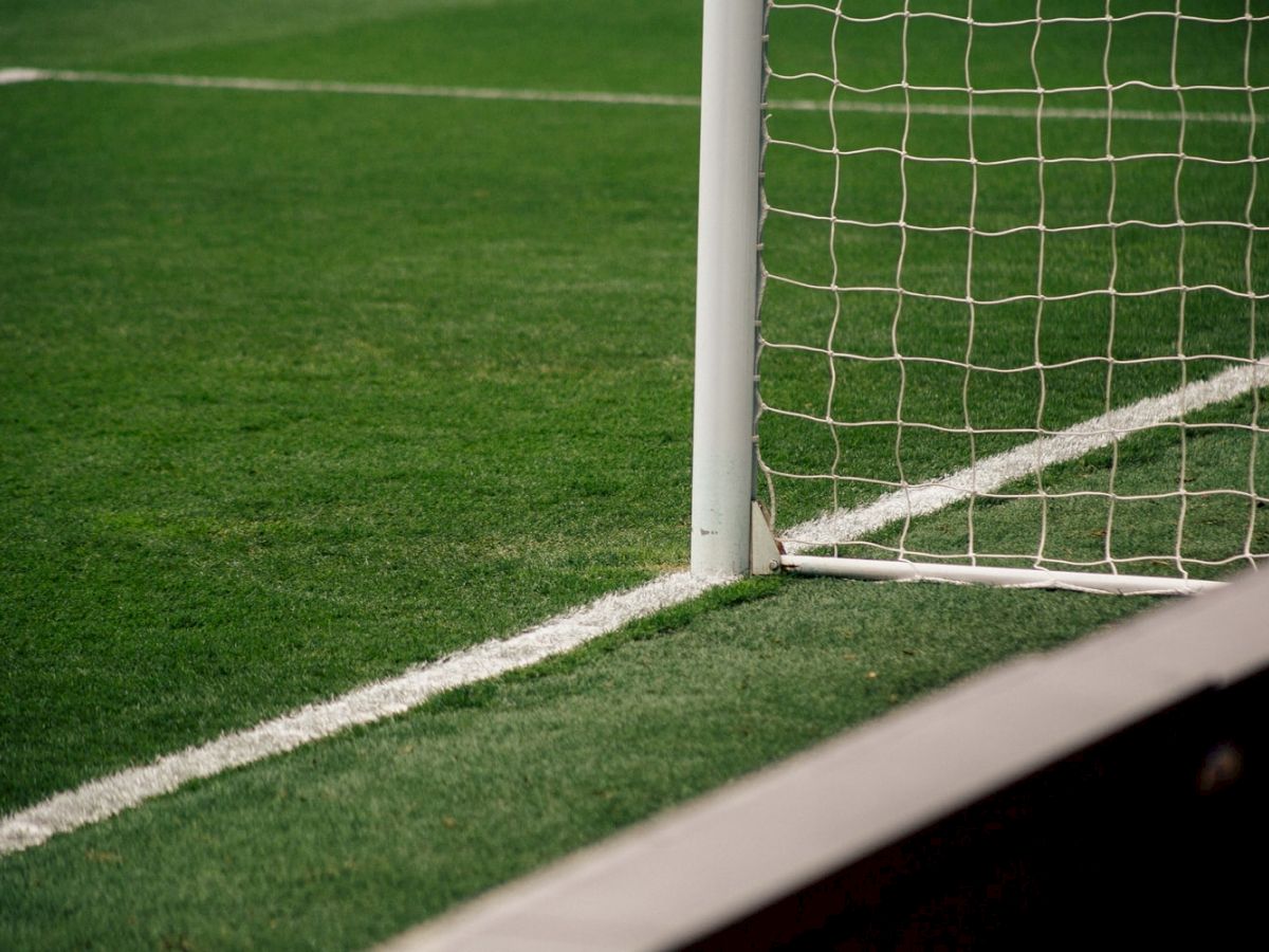 The image shows part of a soccer field with green grass, a goalpost, and a net. The goalpost is positioned at the corner of the field.