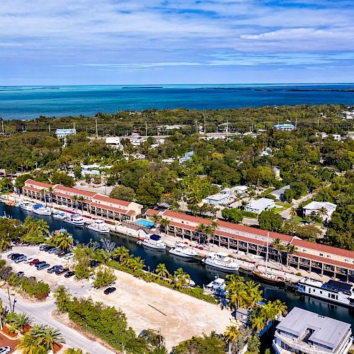 Aerial photo of a coastal town with buildings, a canal, and dense greenery, extending to the ocean in the distance.