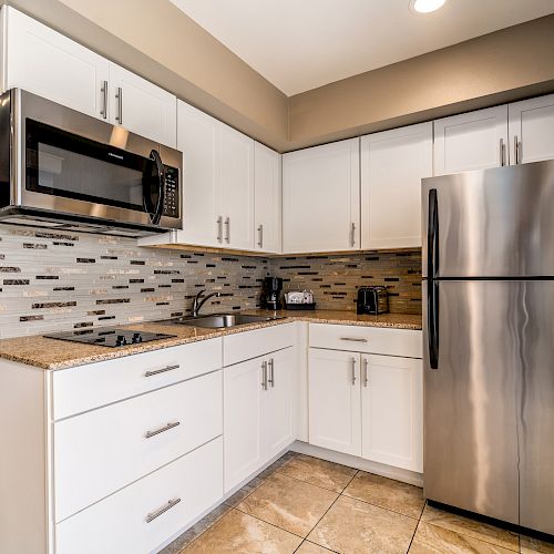 This image shows a modern kitchen featuring white cabinets, a stainless steel refrigerator, microwave, and various small appliances on the countertop.