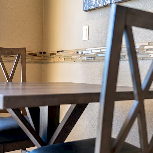 The image shows a close-up of a wooden table and chairs with a metal design in a modern dining area, near a wall and a window.