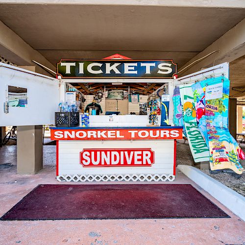 A small ticket booth for snorkeling tours called Sundiver, with colorful signs and maps displayed on the sides, and vending machines nearby.