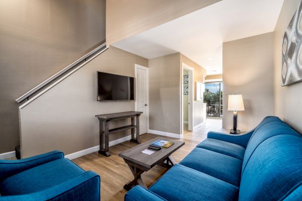 A cozy living room with blue sofas, a wooden coffee table, a wall-mounted TV, and stylish decor elements, including a lamp and artwork.