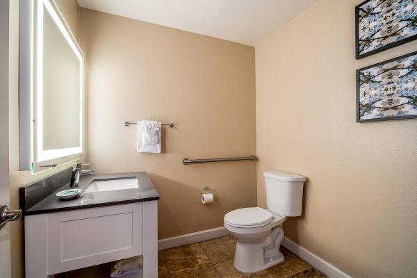 A bathroom with a sink, mirror, toilet, and towel racks, featuring two framed pictures on beige walls and tiled flooring.