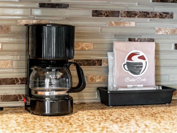 A black drip coffee maker beside a napkin holder on a tiled counter.