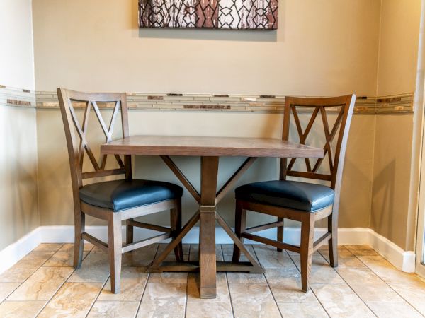 A small dining nook with a wooden table and two matching chairs, set in a corner by tiled floors and a decorative mirror above.