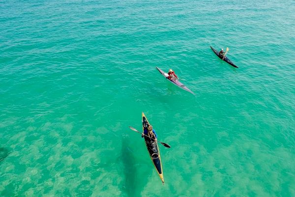 Two people are kayaking on clear turquoise water, creating gentle ripples as they paddle through the serene ocean.