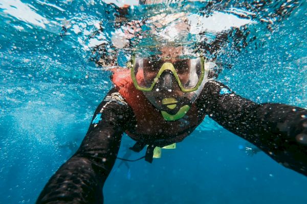 A person snorkeling underwater, wearing a mask and snorkel, captured in a selfie-style photograph with bubbles around.