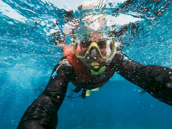 A person snorkeling underwater, wearing a mask and snorkel, captured in a selfie-style photograph with bubbles around.