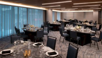 The image shows a banquet hall set up with round tables and chairs, elegantly arranged with place settings, glassware, and centerpieces.