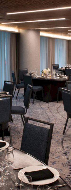 The image shows an elegantly set banquet hall with round tables, black chairs, and folded napkins, ready for an event.