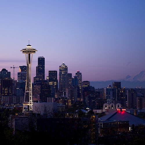 The image shows the Seattle skyline at twilight, featuring the Space Needle prominently with Mount Rainier visible in the background.