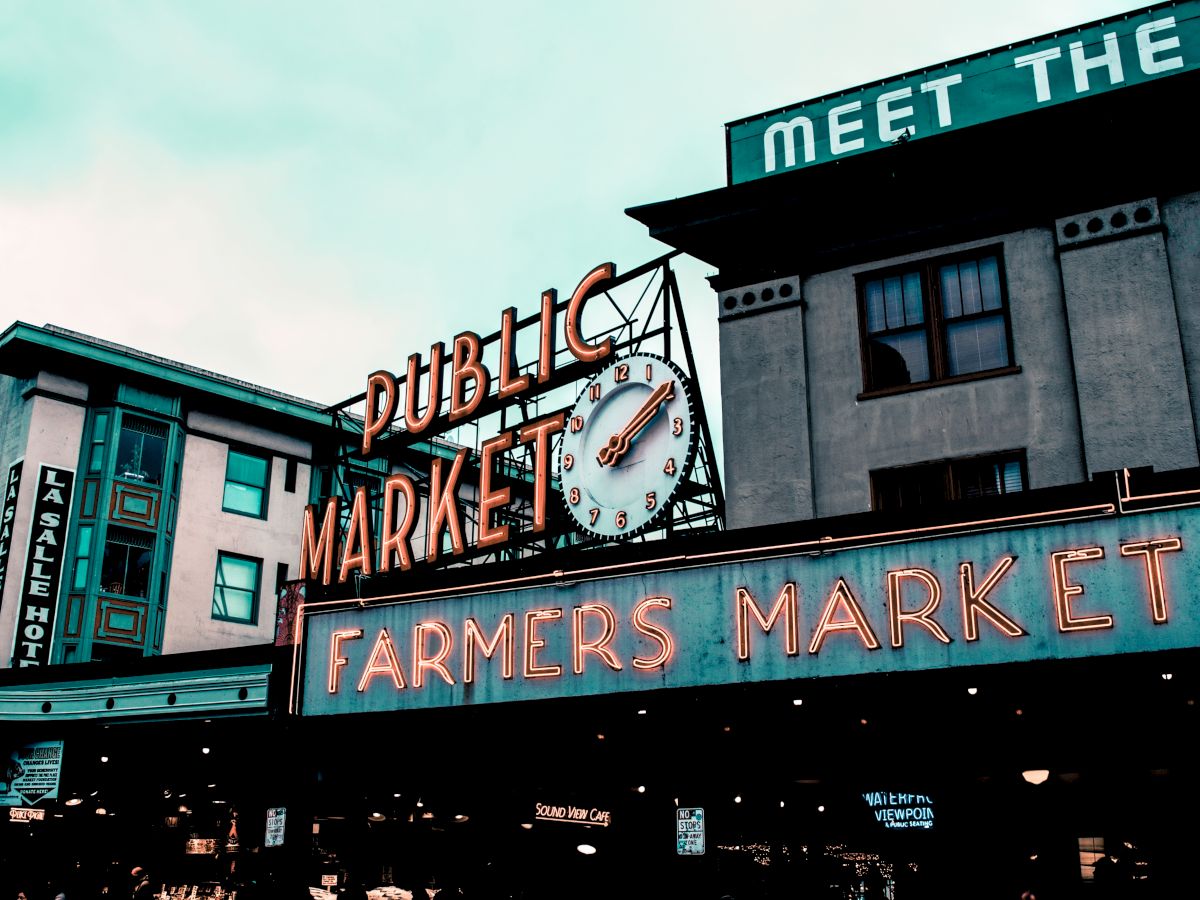 The image shows the exterior of a public market with a large neon sign reading "Public Market" and "Farmers Market" on a building.