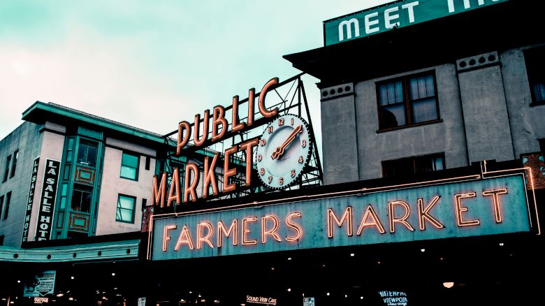 The image shows the exterior of a public market with a large neon sign reading "Public Market" and "Farmers Market" on a building.