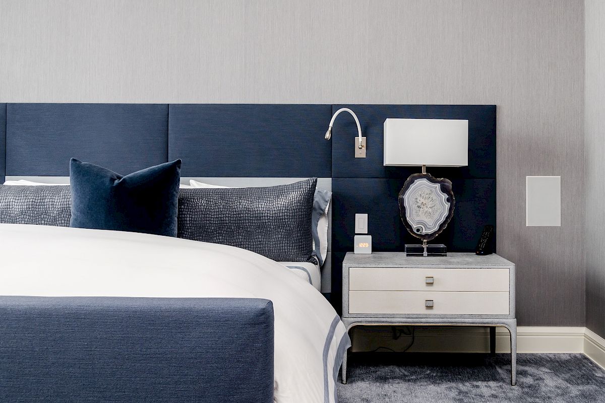 A modern bedroom with a navy blue headboard, white bedding, a nightstand with a lamp, and decorative accents, creating a clean and elegant look.