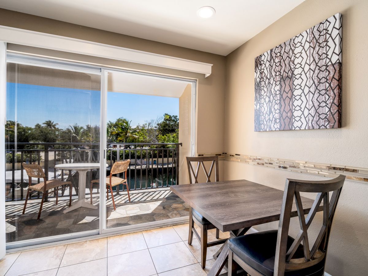 A small dining area with two chairs and a table by a glass sliding door leading to a balcony with two chairs and an open view.